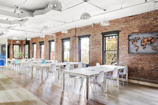 An office with white tables and chairs arranged in front of a brick wall, creating a professional and modern workspace.