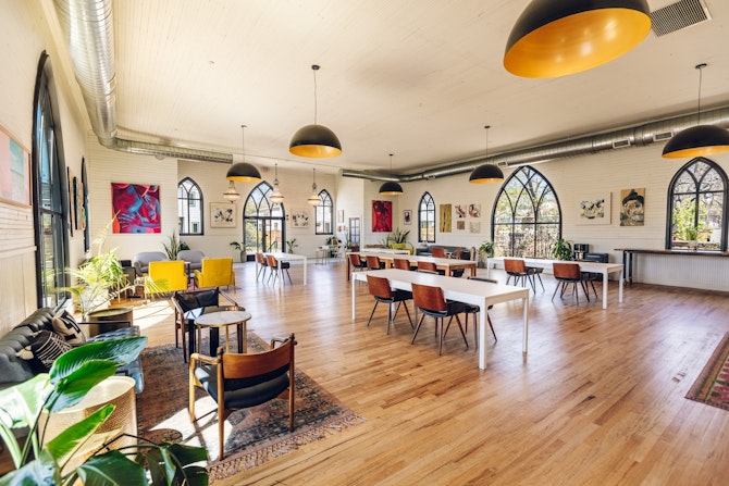 A spacious room filled with numerous tables and chairs for coworking and events.